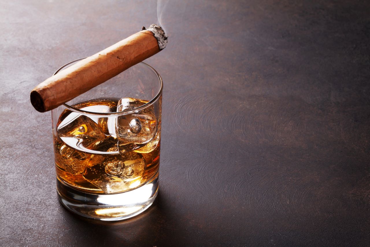 cigarro encendido sentado encima de un vaso de whisky