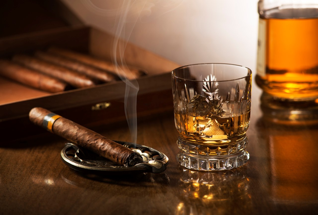 Sklenice whisky s kostkami ledu a kouření doutníku na dřevěný stůl